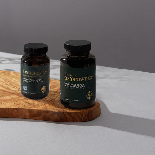 Oxy-Powder 120 capsules and Latero Flora 60 capsules bottles on a wooden board, making up the Global Healing Colon Cleanse Program