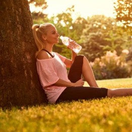 Woman sat against a tree drinking water